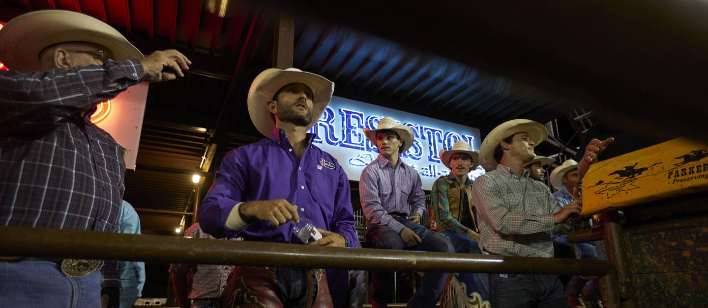 Man surrounded by people on the bucking chutes at a rodeo getting ready to ride bulls.